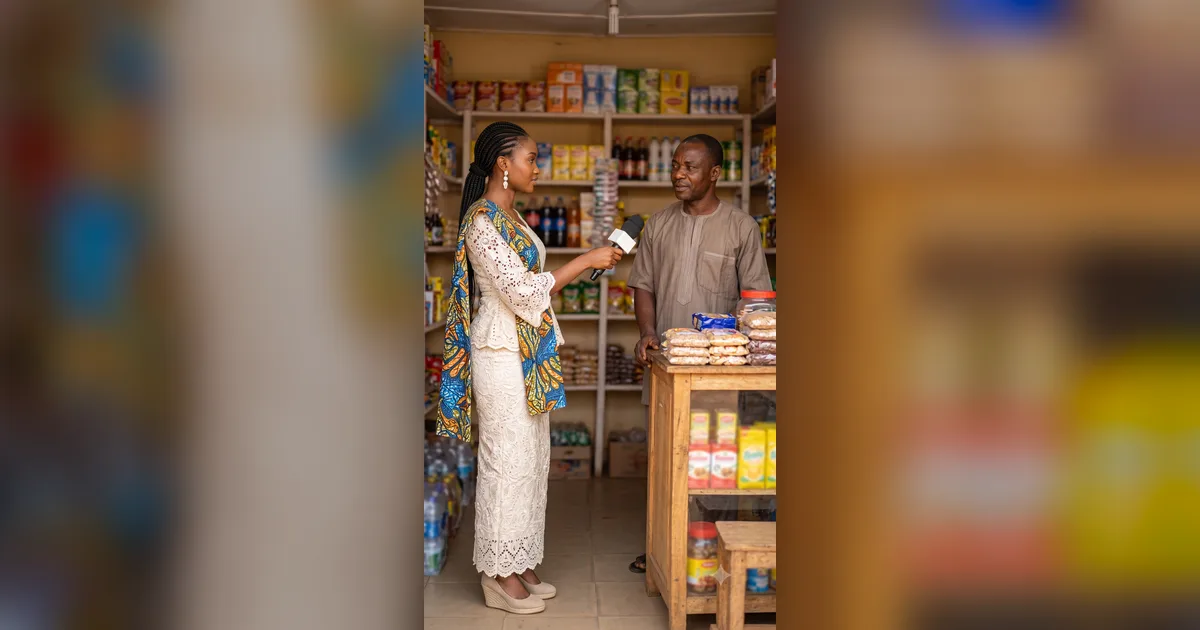 Une journaliste tend un micro à un commerçant derrière le comptoir de sa boutique camerounaise